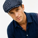 Man wearing a navy blue cap with white polka dots and a matching navy shirt on a light gray background