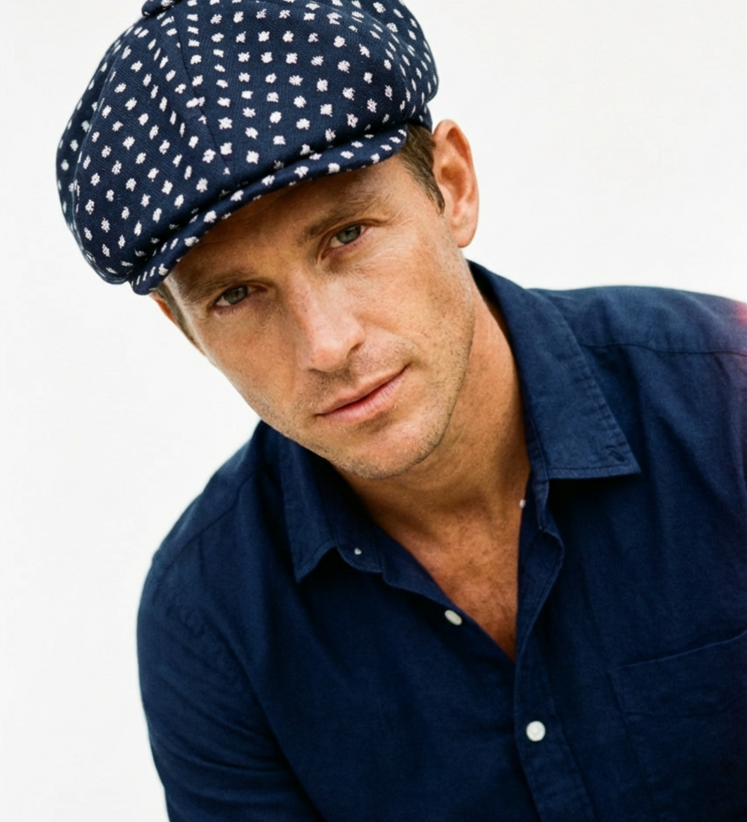 Man wearing a navy blue cap with white polka dots and a matching navy shirt on a light gray background