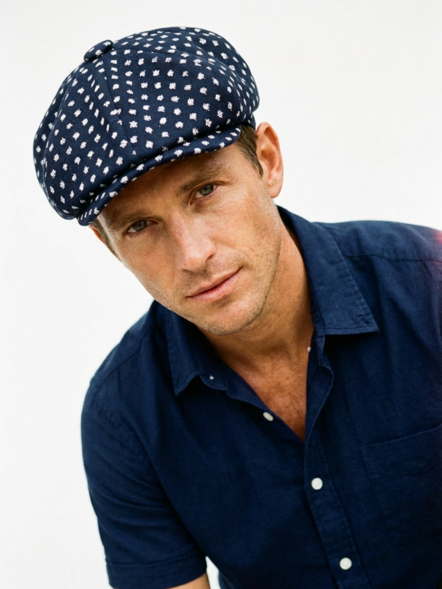 Man wearing a navy blue cap with white polka dots and a matching navy shirt on a light gray background