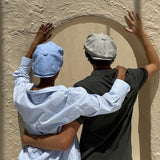 a man and a woman wearing Bakerboy caps in Irish linen herringbone — Riley Skies by Mister Miller, a breathable summer hat handmade in Britain. 