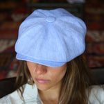 A woman wearing a Bakerboy cap in light blue Irish linen herringbone — Riley Skies by Mister Miller, a breathable summer hat handmade in Britain. side view