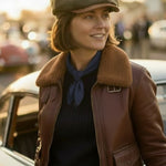 WOMAN WEARING A RACING GREEN BAKERBOY CAP AND A BROWN BOMBER JACKET BESIDE A CLASSIC CAR