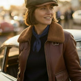 WOMAN WEARING A RACING GREEN BAKERBOY CAP AND A BROWN BOMBER JACKET BESIDE A CLASSIC CAR