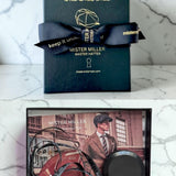 Mister Miller hat box with a bow and image of a tape measure on a card featuring a man wearing a hat