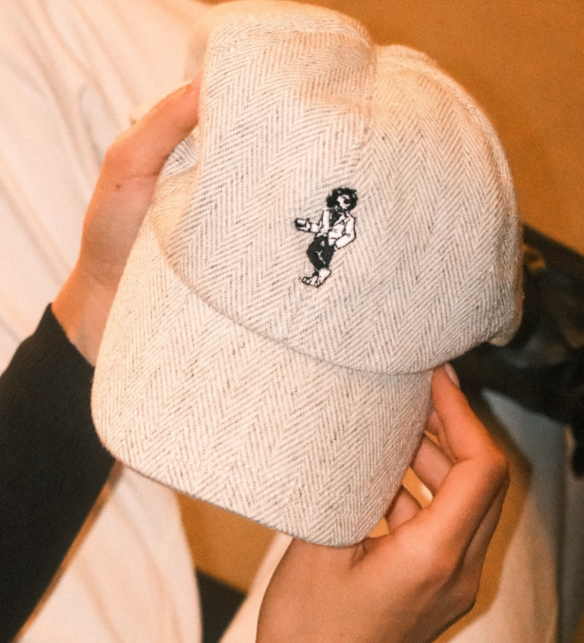Beige wool baseball cap with lion embroidery. Held in the hands of a woman. A limited-edition Mister Miller x Gentleman’s Racer collaboration.