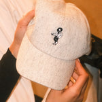 Beige wool baseball cap with lion embroidery. Held in the hands of a woman. A limited-edition Mister Miller x Gentleman’s Racer collaboration.