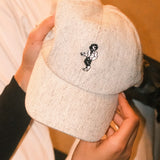 Beige wool baseball cap with lion embroidery. Held in the hands of a woman. A limited-edition Mister Miller x Gentleman’s Racer collaboration.