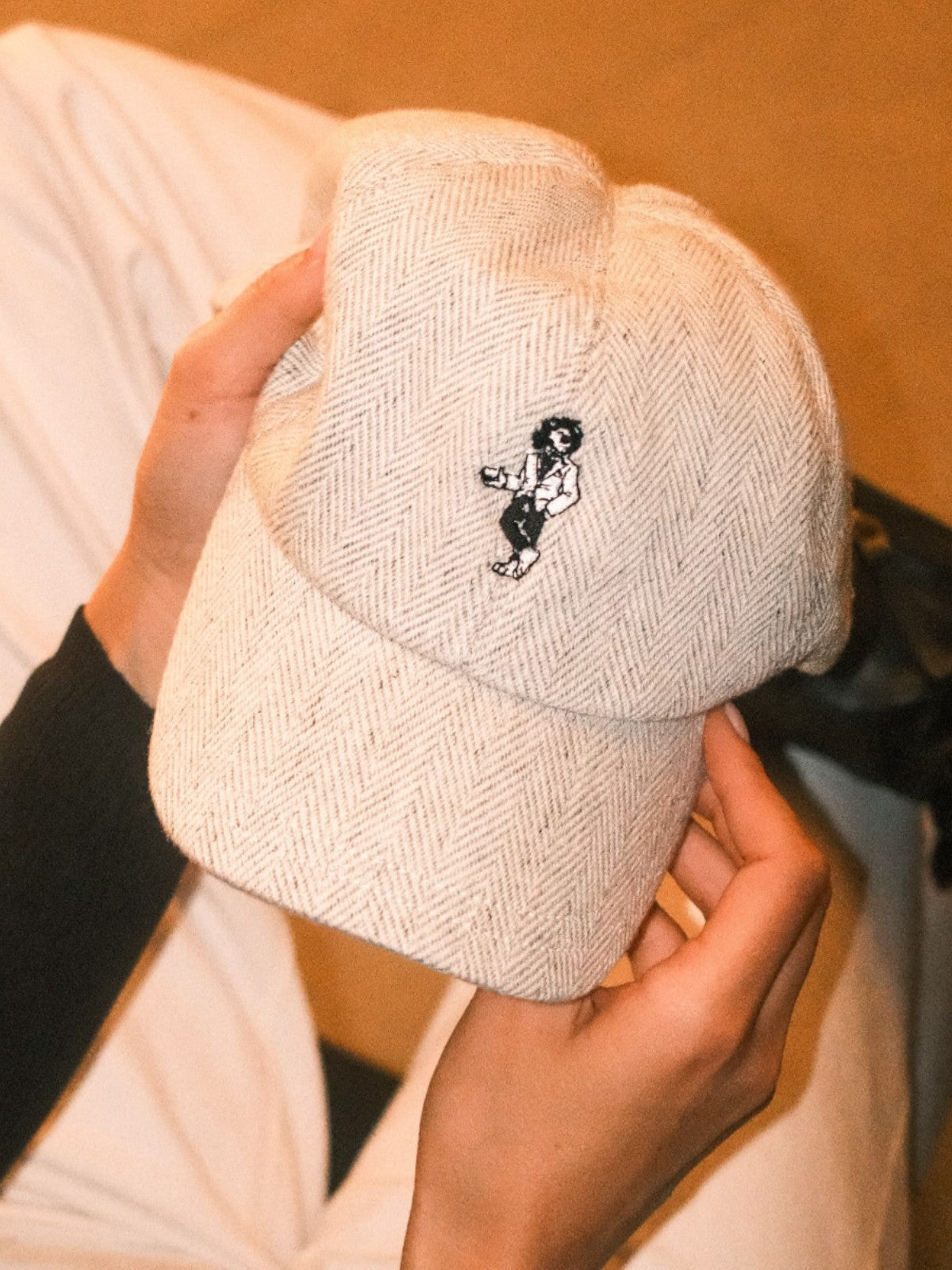Beige wool baseball cap with lion embroidery. Held in the hands of a woman. A limited-edition Mister Miller x Gentleman’s Racer collaboration.