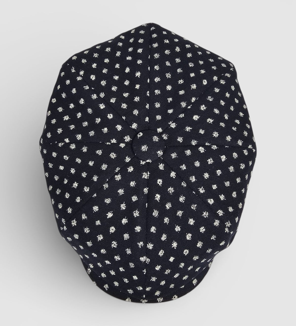 Navy Bakerboy cap with white polka dots on a grey background