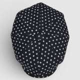 Navy Bakerboy cap with white polka dots on a grey background