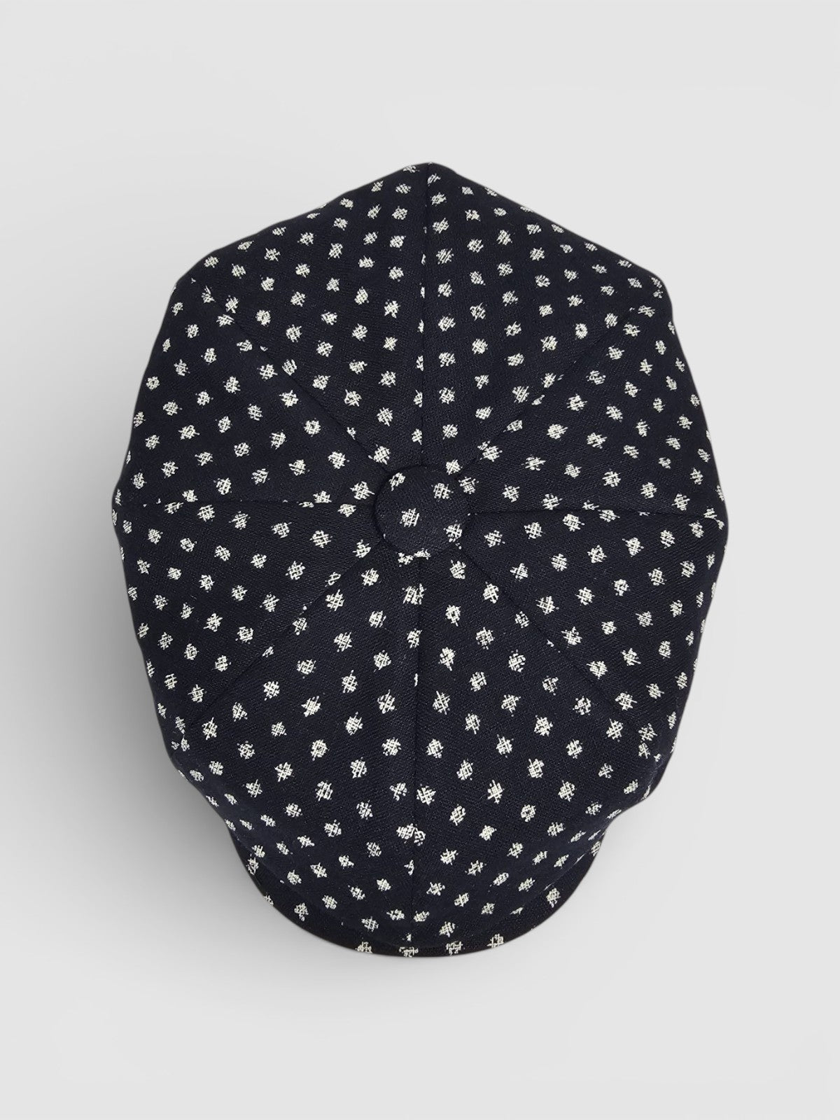 Navy Bakerboy cap with white polka dots on a grey background