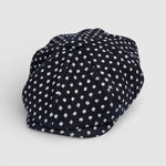 Navy Bakerboy cap with white textured polka dots on a grey background