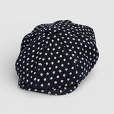 Navy Bakerboy cap with white textured polka dots on a grey background