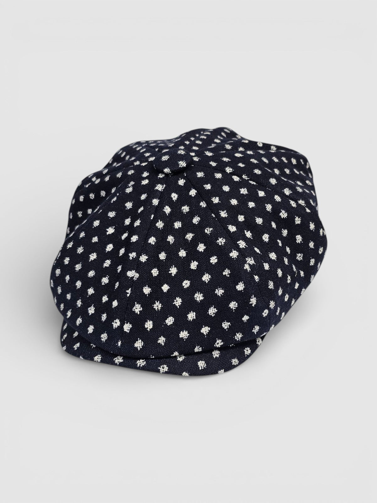 Navy Bakerboy cap with white textured polka dots on a grey background