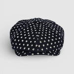 Navy Bakerboy cap with white polka dots on a grey background