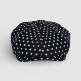 Navy Bakerboy cap with white polka dots on a grey background