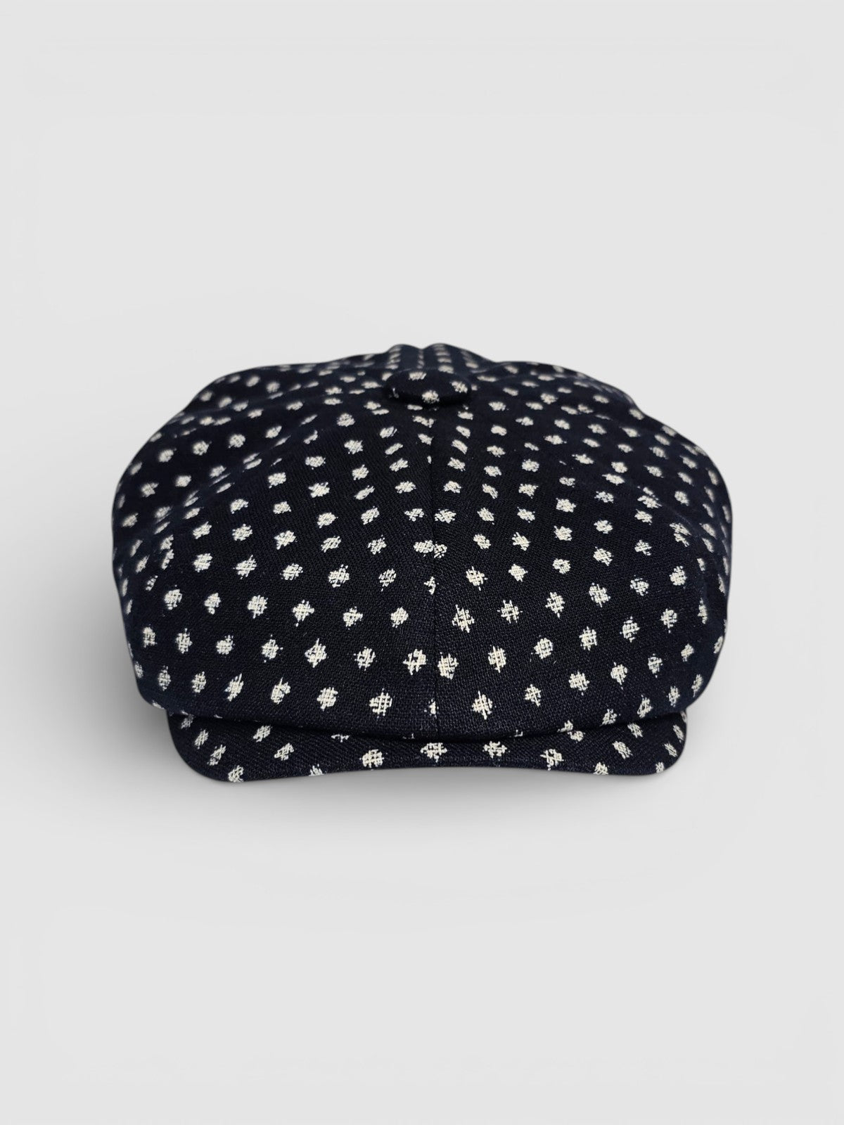 Navy Bakerboy cap with white polka dots on a grey background