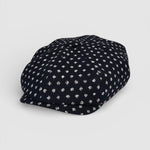 Navy Bakerboy cap with white polka dots on a grey background angle view