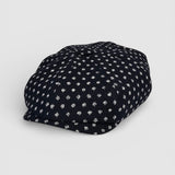Navy Bakerboy cap with white polka dots on a grey background angle view