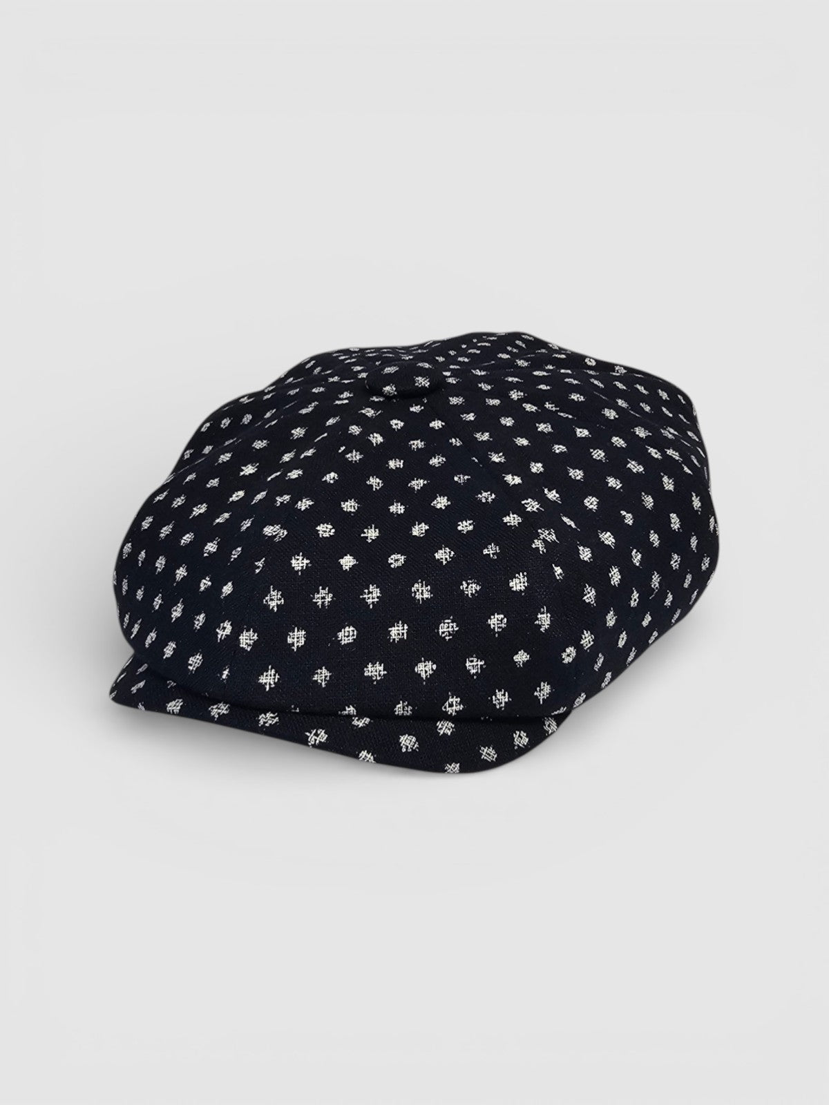 Navy Bakerboy cap with white polka dots on a grey background angle view