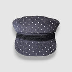 Navy blue cap with white polka dots and a black band on a light gray background