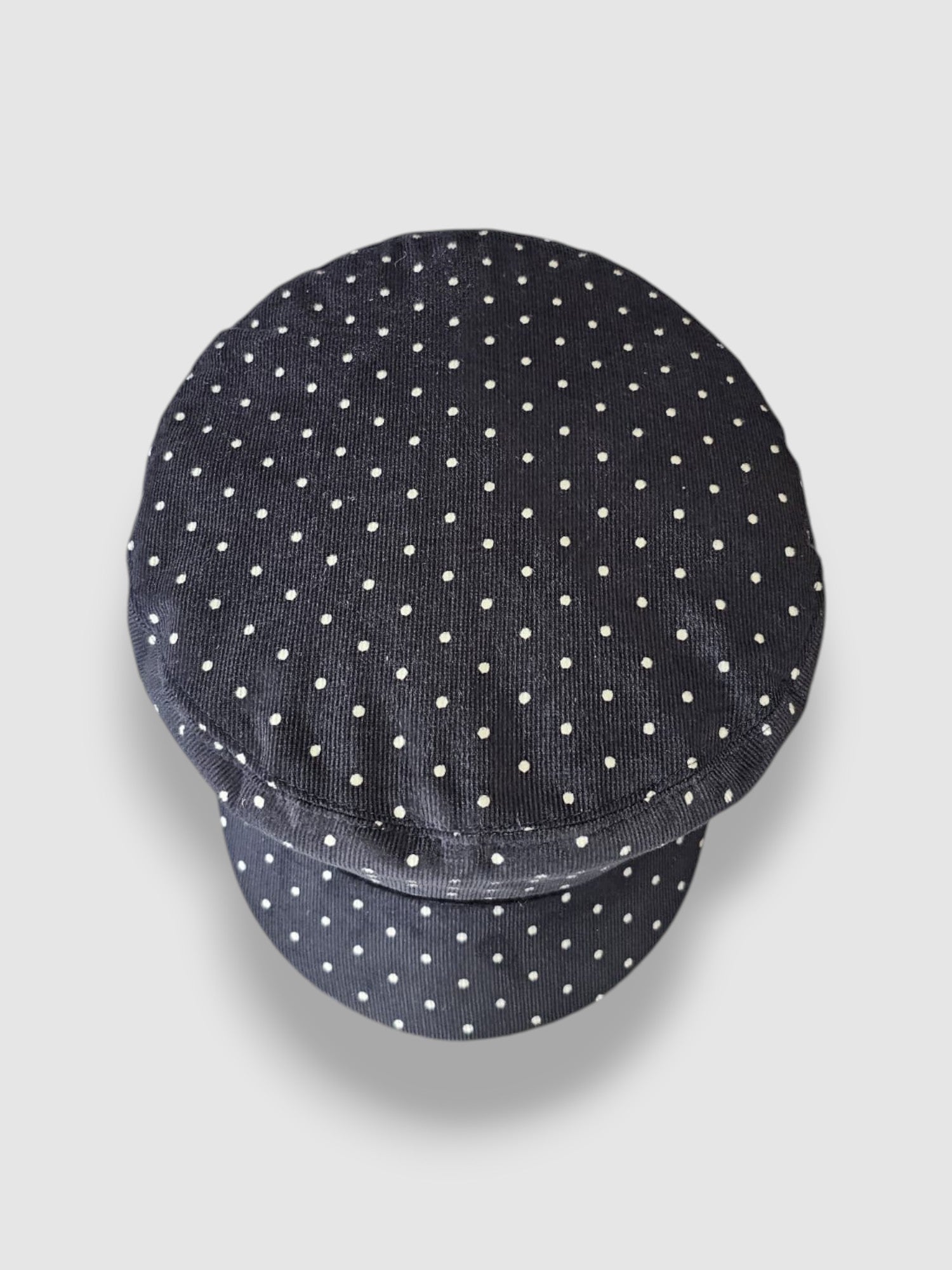 Navy blue cap with white polka dots on a light gray background