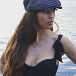 Woman wearing a navy polka dot cap and black dress by a body of water.