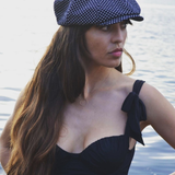 Woman wearing a navy polka dot cap and black dress by a body of water.
