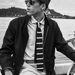 Man wearing a cap, sunglasses, and a striped tie on a boat with a scenic background