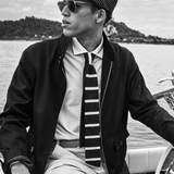 Man wearing a cap, sunglasses, and a striped tie on a boat with a scenic background