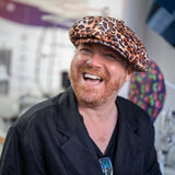 Leigh Francis wearing leopard print velvet Bakerboy hat — oversized 90s-inspired cap with curved peak and signature 70s cartoon lining from his collaboration with Mister Miller.